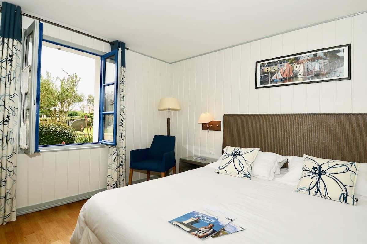 A hotel room with a bed, a chair, a lamp, and a window with curtains.