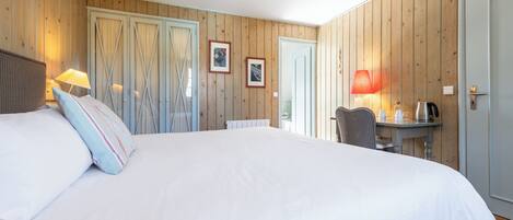 Un dormitorio con una cama grande, paredes de madera, un escritorio con lámpara y una puerta.