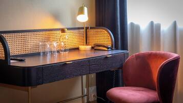 Una habitación de hotel con escritorio, lámpara, silla y ventana con cortinas.