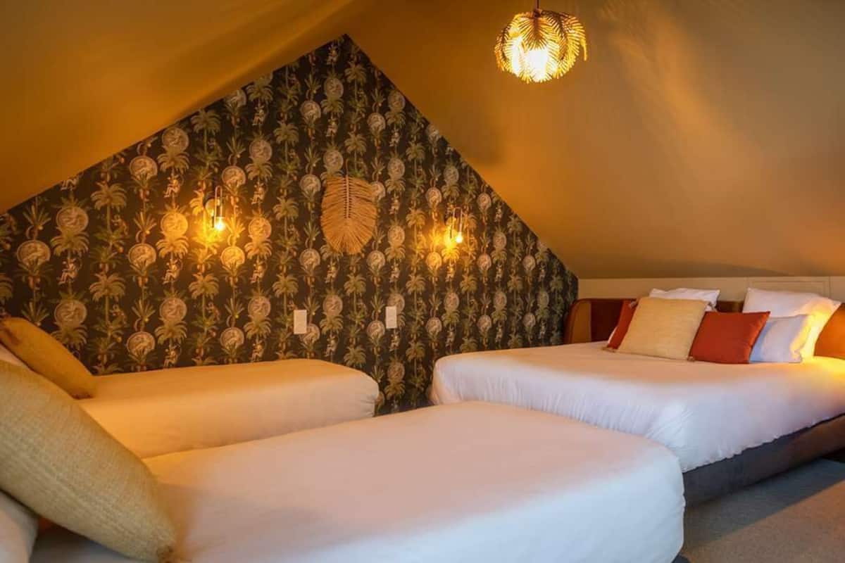 Una habitación acogedora con dos camas, un detalle decorativo en la pared y una lámpara de techo original.