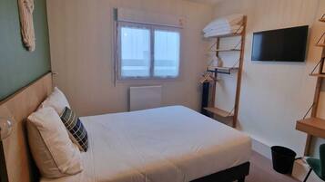 Un dormitorio con cama, escritorio, silla, televisor, ventana y lámpara colgante.