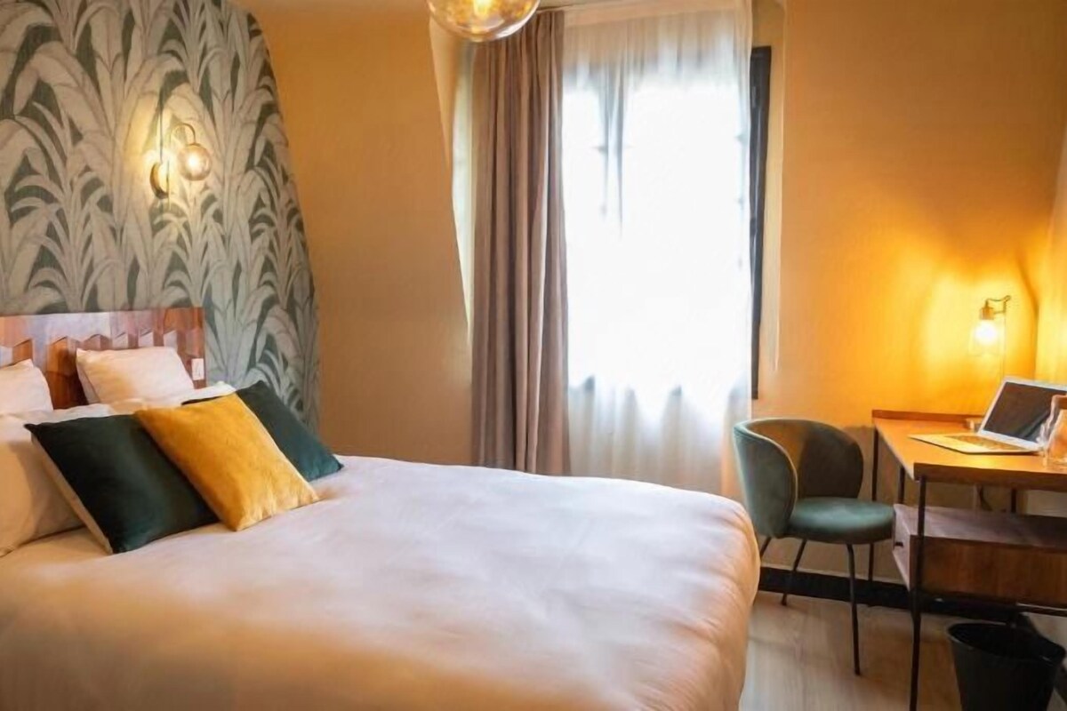 A hotel room with a large bed, two bedside lamps, a desk with a laptop, and a chair.
