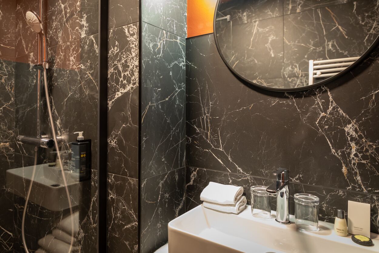Un baño con lavamanos de mármol, un espejo y una zona de ducha.