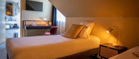 A hotel room with a bed, bedside table, lamp, and a desk with a chair.