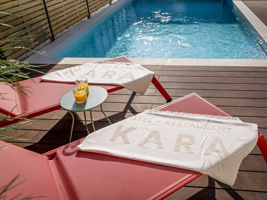 A poolside area with lounge chairs and a table with a beverage.