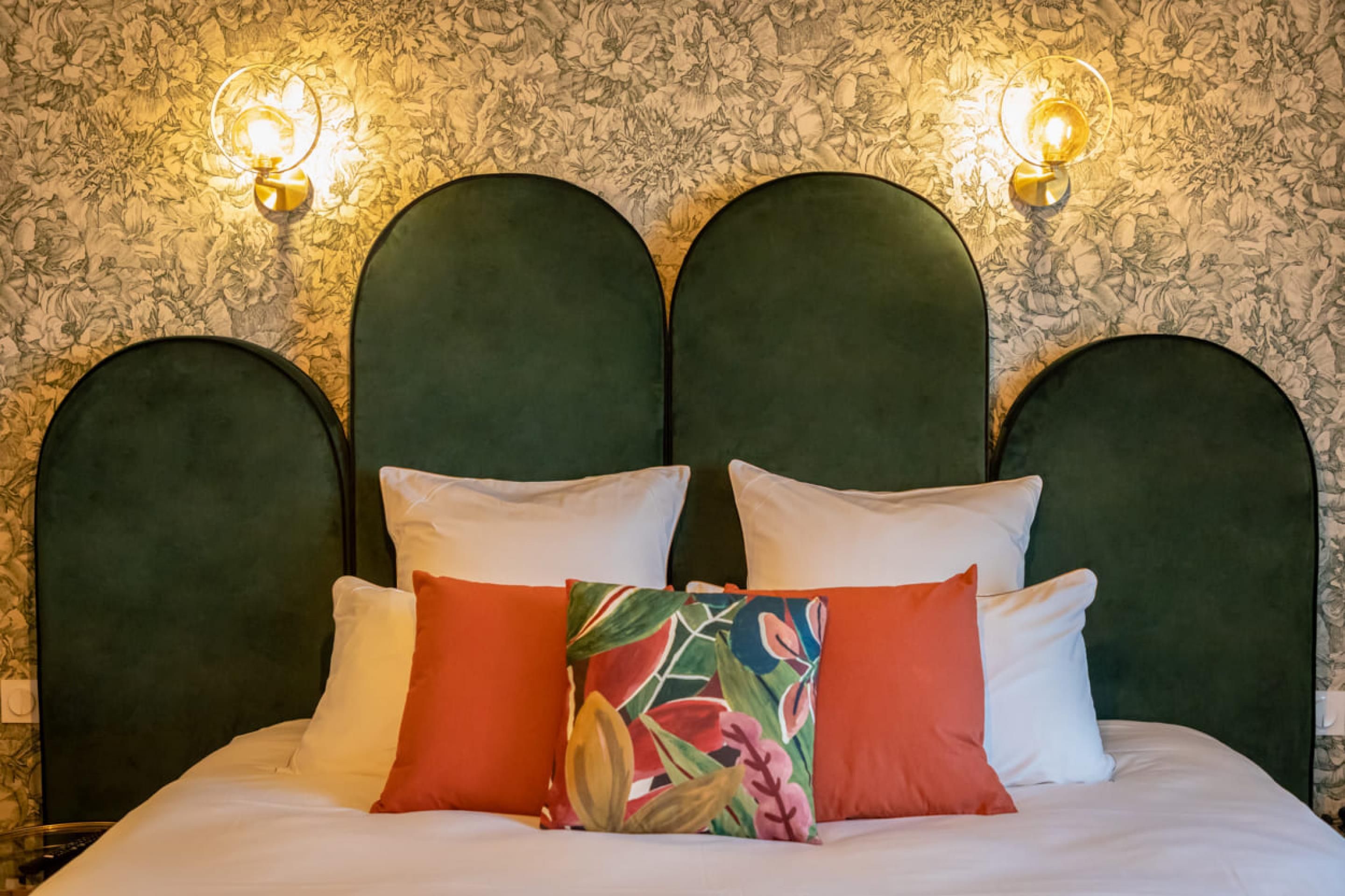 Un letto con una testiera imbottita verde, biancheria da letto bianca e numerosi cuscini di vari colori.