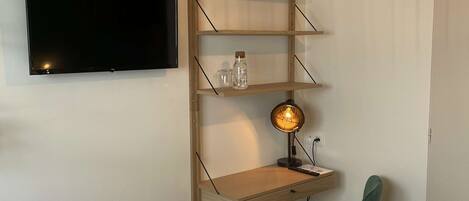 Een slaapkamer met een bed, een bureau met stoel, een televisie, een lamp en een wandplank.
