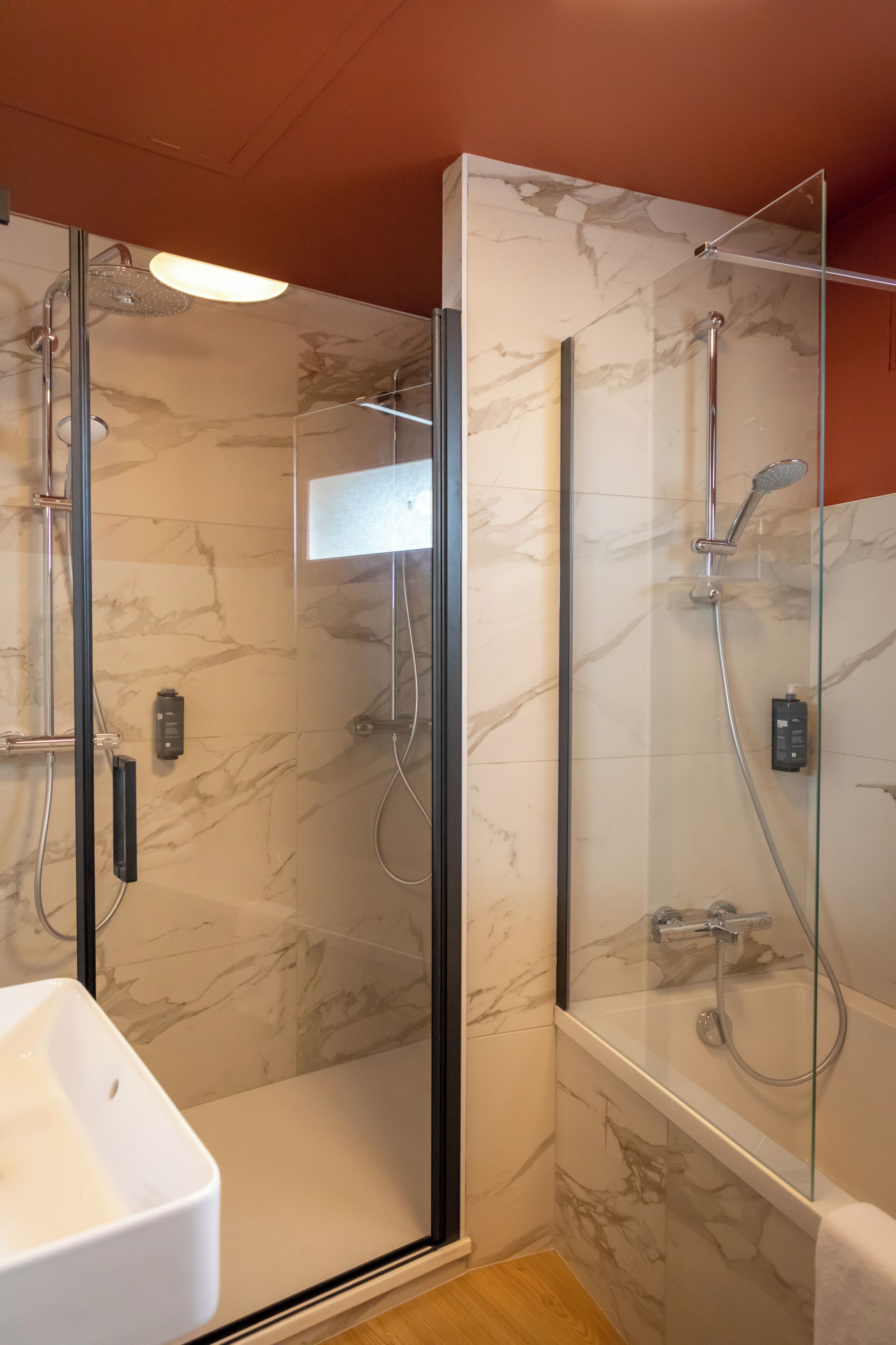 A modern bathroom with a glass-enclosed shower, a white sink, and marble walls.