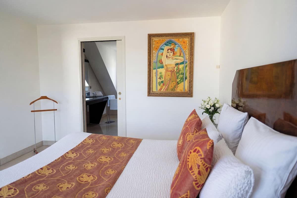 A bedroom with a bed, a painting, and a staircase leading to a balcony.