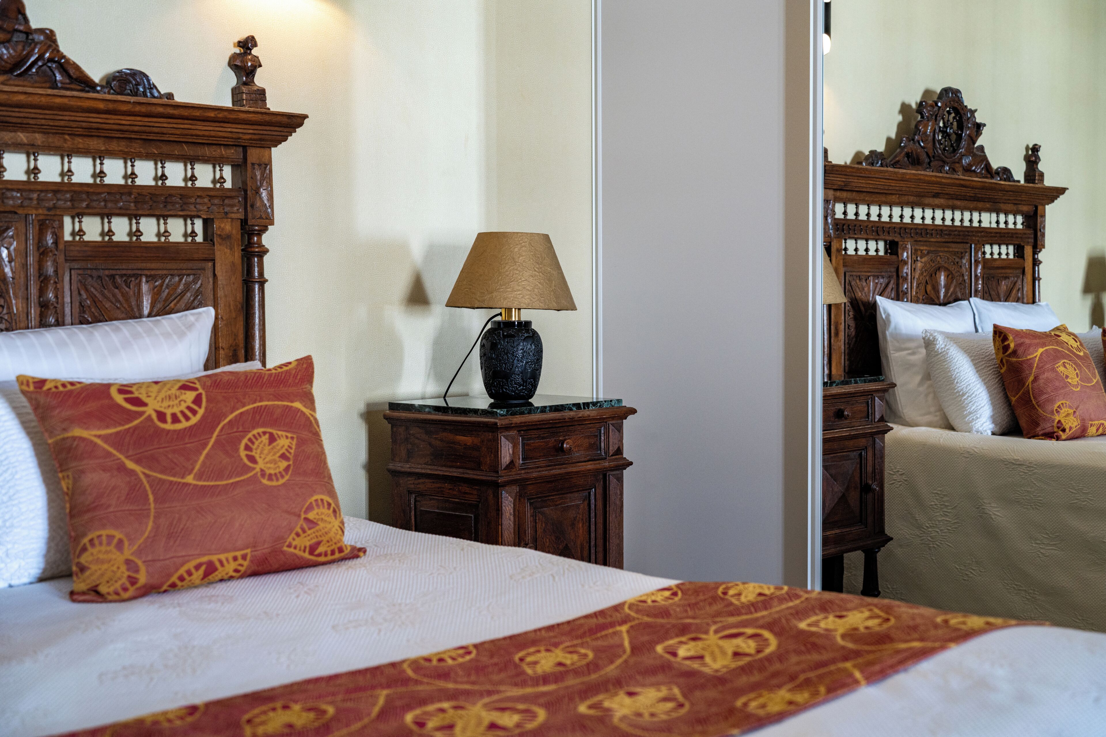 A hotel room with a large bed, a nightstand with a lamp, and a mirror reflecting the room's decor.