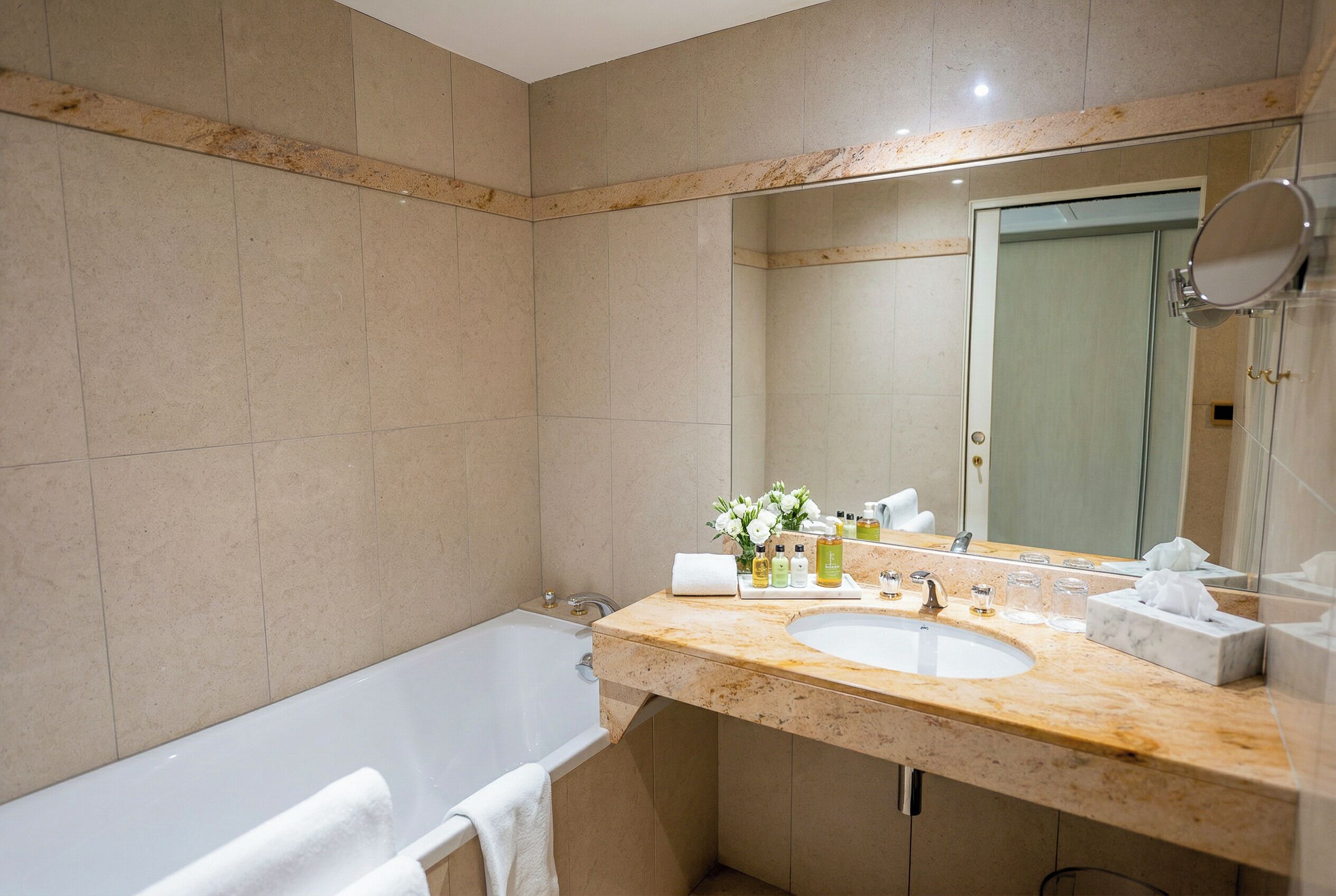Un baño moderno con una bañera, un lavabo con artículos de aseo y un espejo grande.