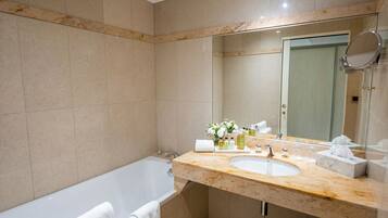 Un baño moderno con una bañera, un lavabo con artículos de aseo y un espejo grande.