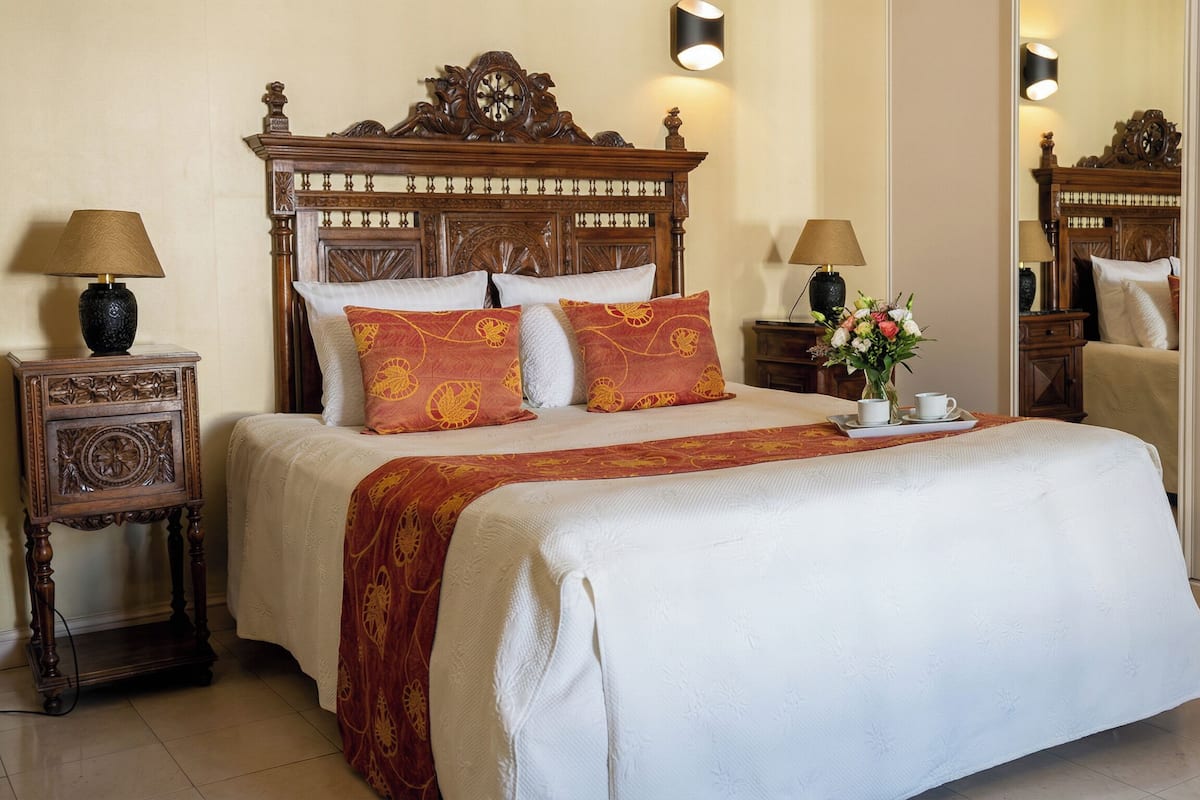 A hotel room with a large bed, two bedside tables, a nightstand, a mirror, and a vase with flowers.