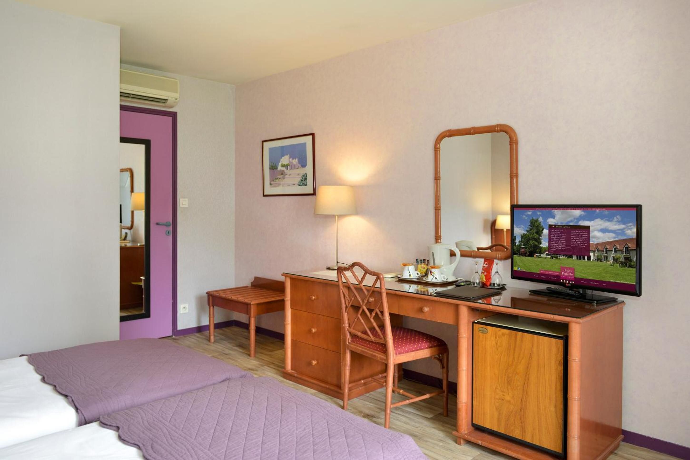 A hotel room with a bed, a desk with a chair, a television, and a mirror.