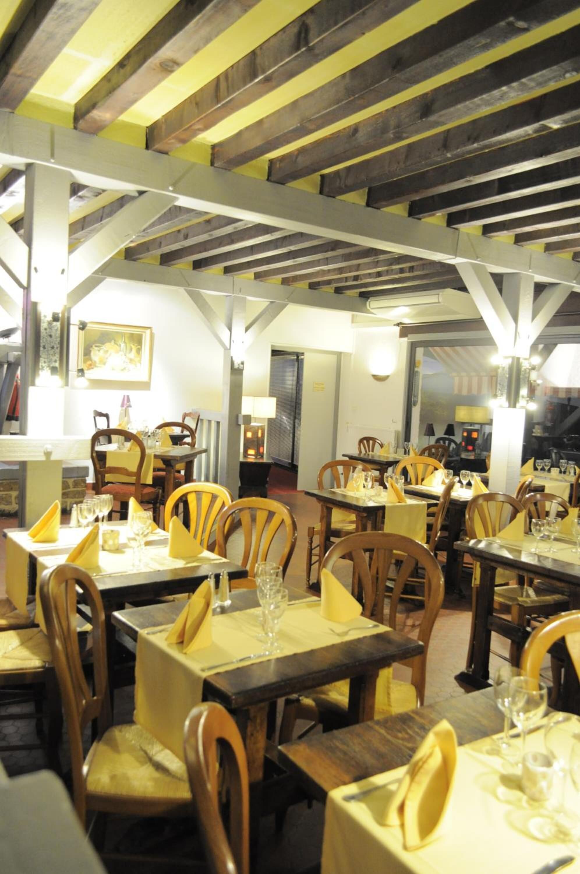 Ein Restaurant mit Holztischen und -stühlen, gelben Tischdecken und einer hohen Decke mit freiliegenden Balken.