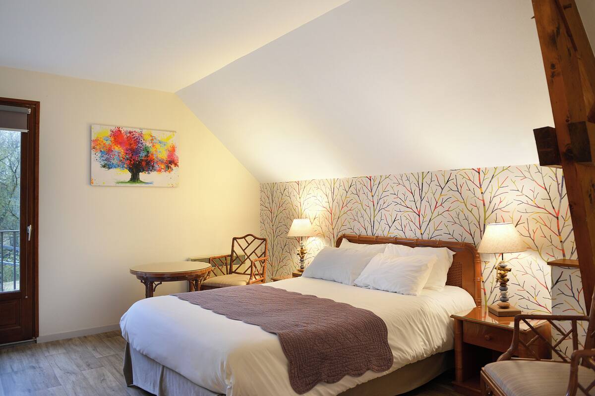 A bedroom with a large bed, two bedside tables with lamps, a chair, and a window.