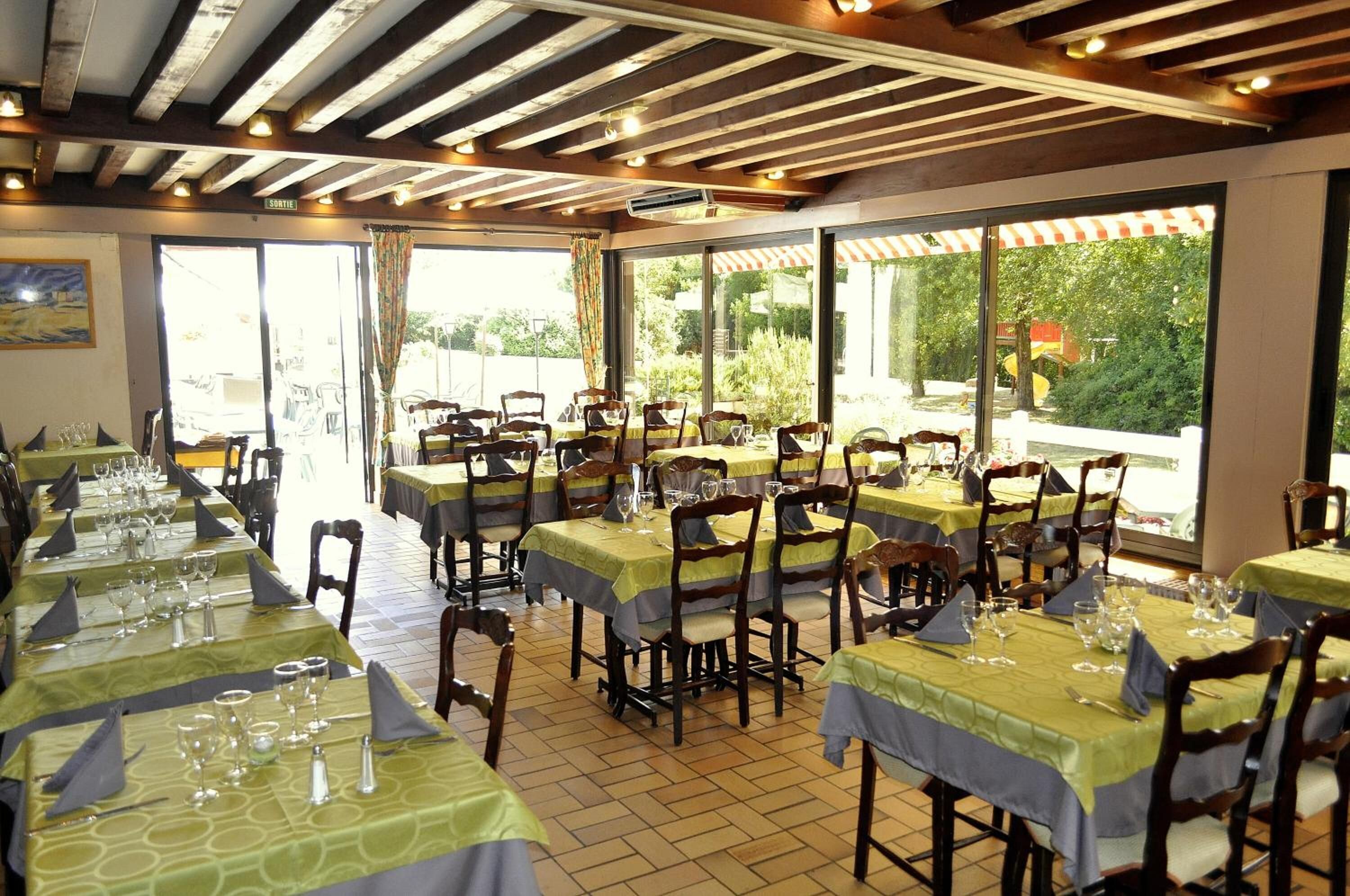A restaurant with multiple tables set for dining, featuring a wooden ceiling and large windows offering a view of the outdoors.