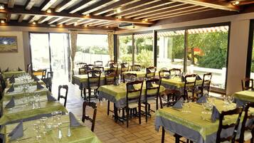 A restaurant with multiple tables set for dining, featuring a wooden ceiling and large windows offering a view of the outdoors.