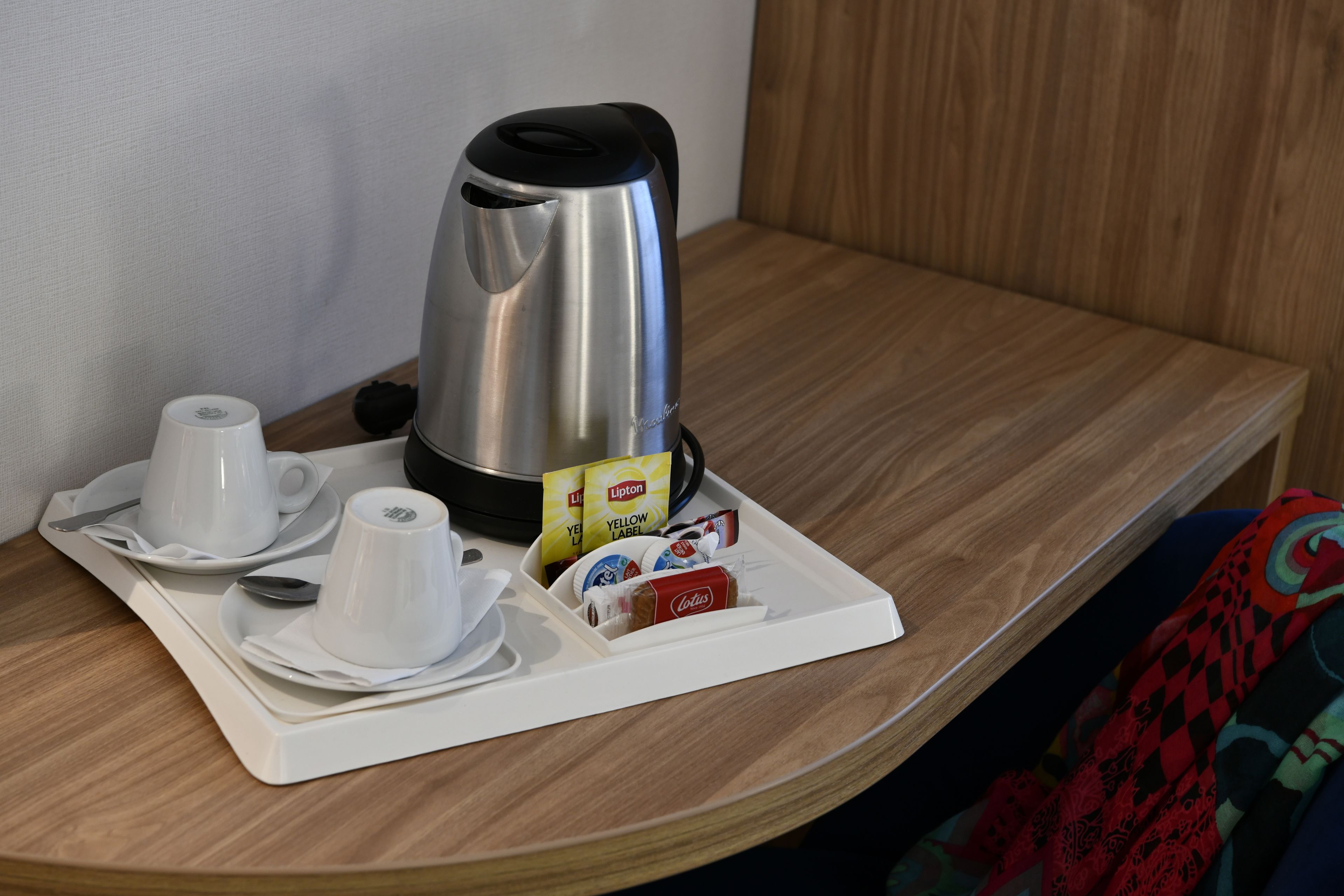 A neatly arranged breakfast tray with a stainless steel coffee maker, two white cups, a spoon, and a small tray with Lipton tea bags and a Coca-Cola can.