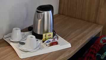 A neatly arranged breakfast tray with a stainless steel coffee maker, two white cups, a spoon, and a small tray with Lipton tea bags and a Coca-Cola can.