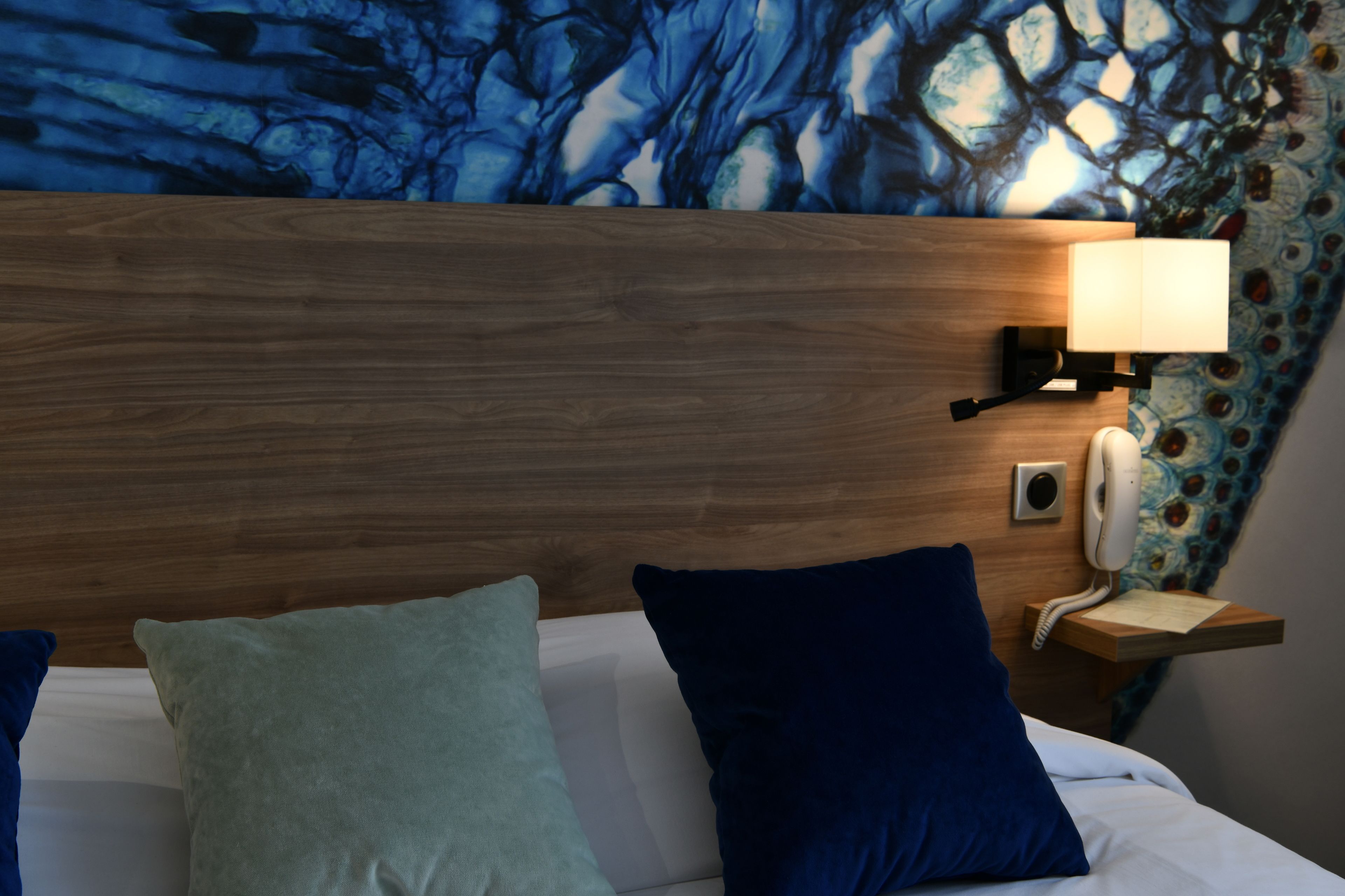A hotel room with a wooden headboard, a bedside lamp, a telephone, and two pillows.