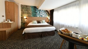 A hotel room with a large bed, a wooden wardrobe, a patterned carpet, and a breakfast tray on the side table.
