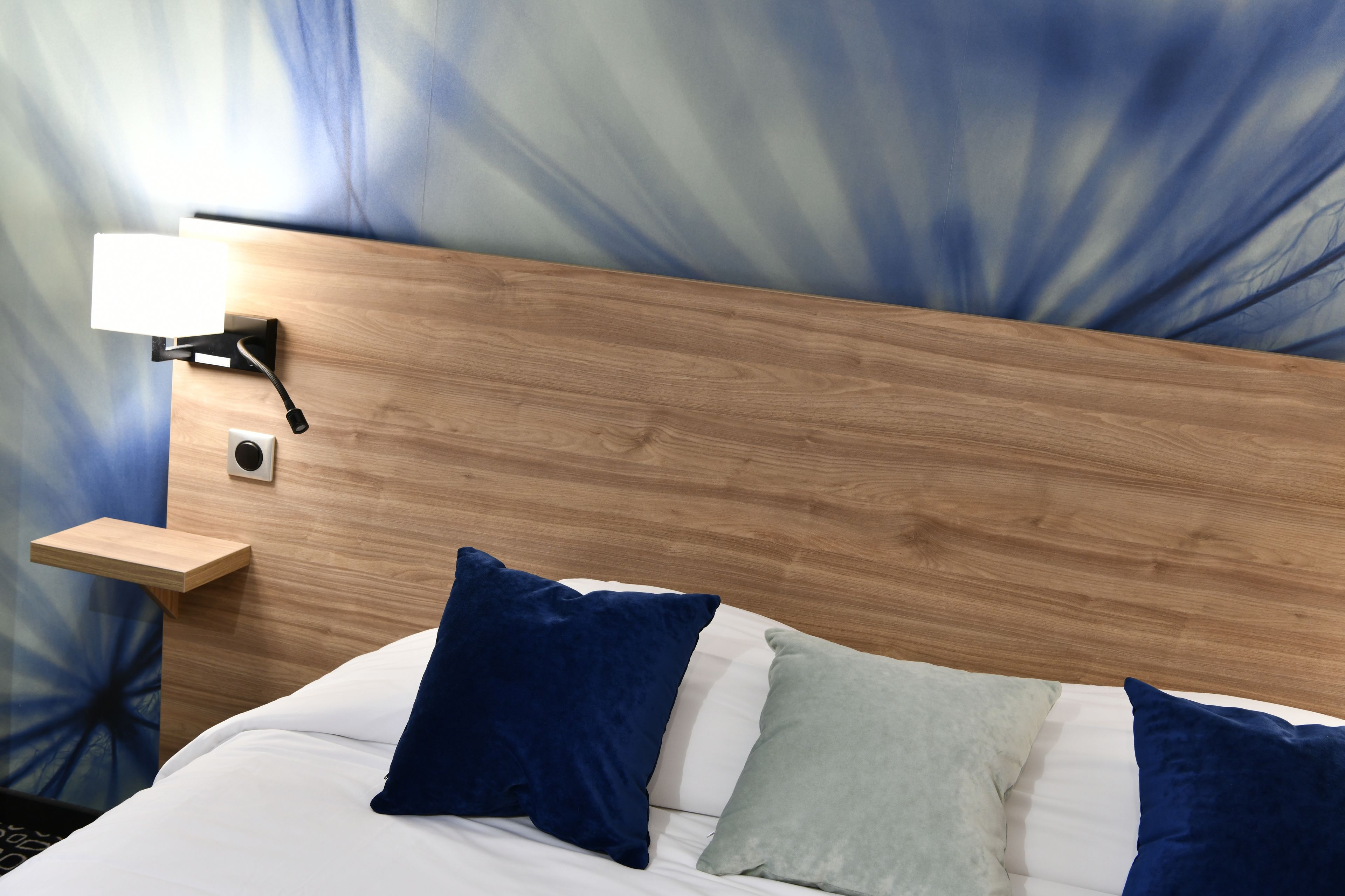 A neatly made bed with blue and white pillows, a wooden headboard, and a bedside table with a lamp.