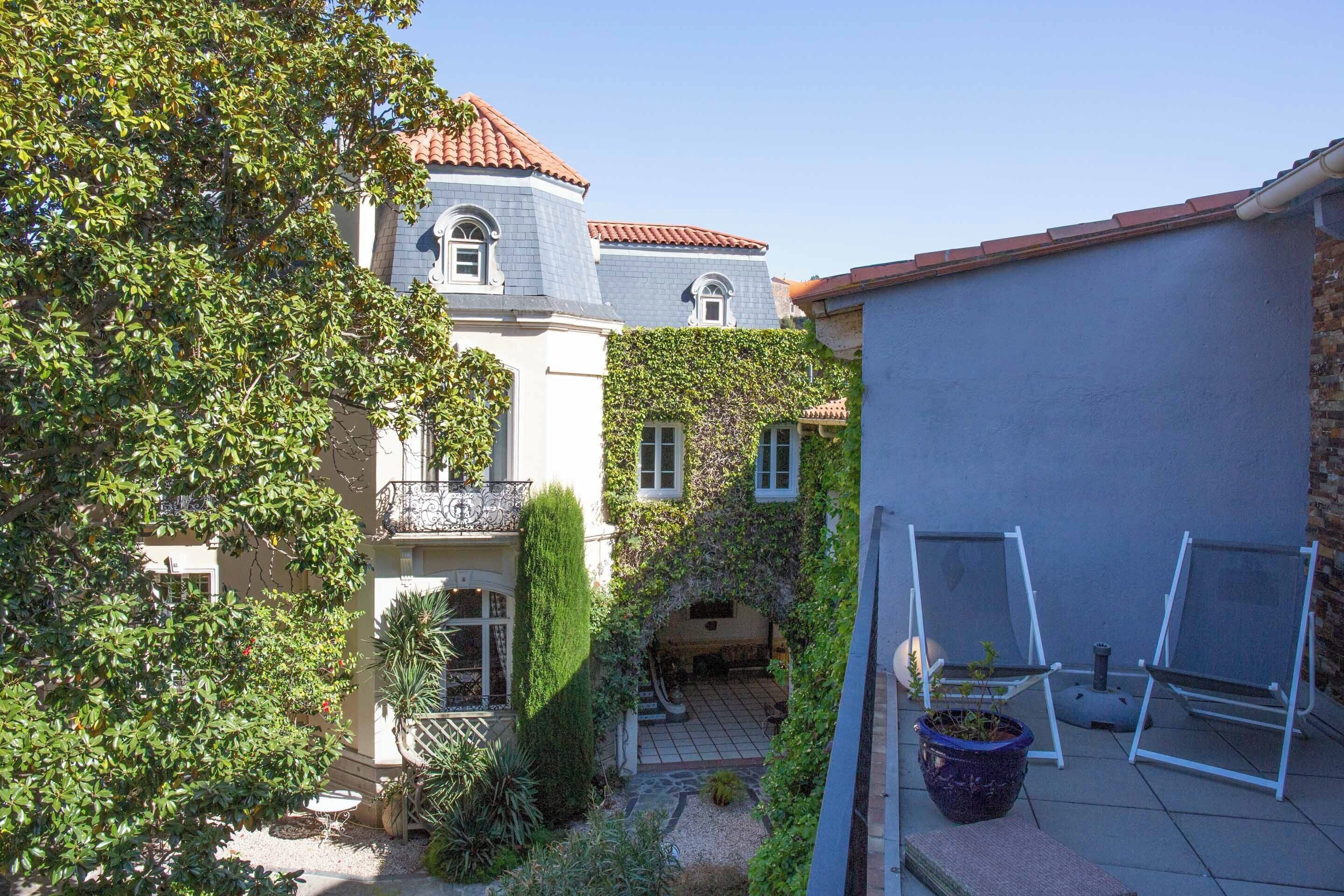 Une cour avec une terrasse carrelée, un pot de fleurs et une chaise en métal.