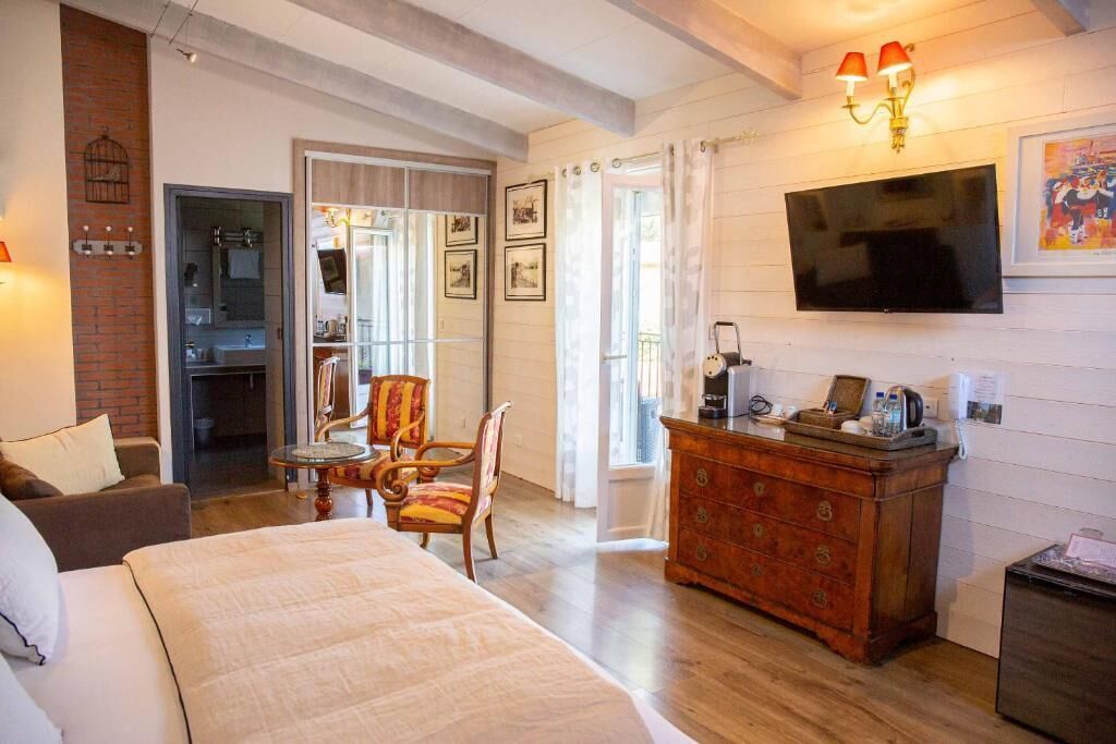 A hotel room with a bed, a wooden dresser, a television, and a bathroom visible through an open door.