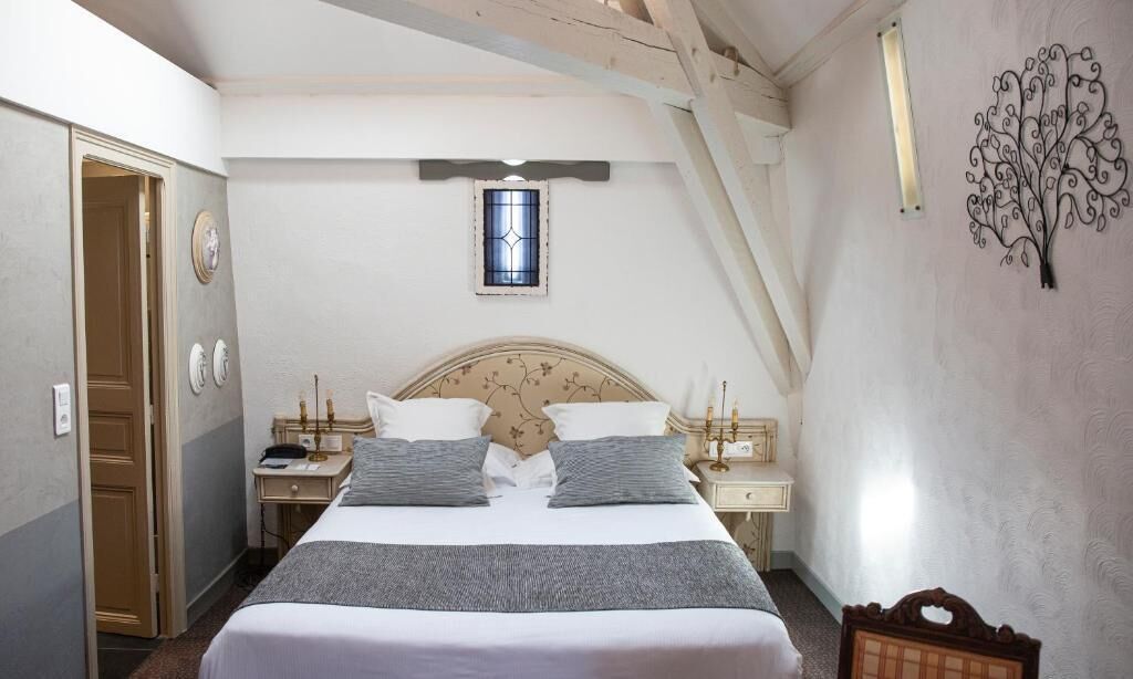 A bedroom with a bed, bedside tables, a nightstand, a window, and a decorative wall piece.