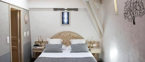A bedroom with a bed, bedside tables, a nightstand, a window, and a decorative wall piece.