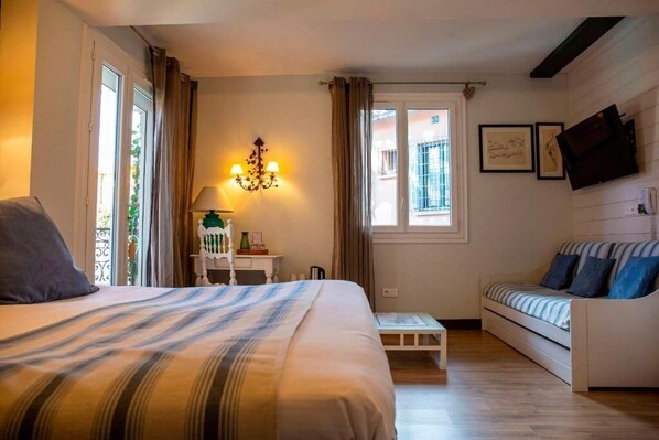 Un dormitorio con una cama, un sofá, una mesita, una lámpara y un televisor en la pared.
