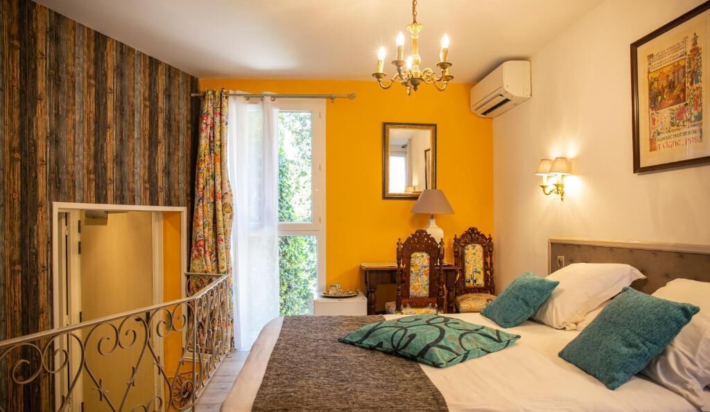 Une chambre à coucher avec un lit, un lustre, un miroir et une fenêtre avec des rideaux.