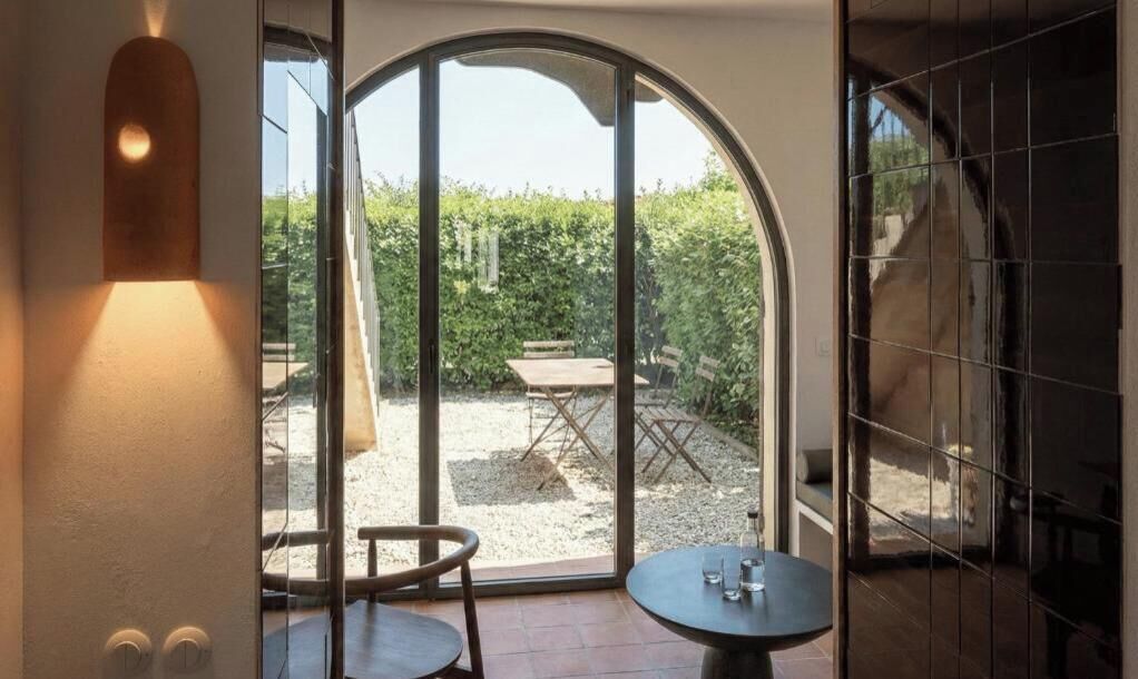 Une pièce dotée d’une grande porte en verre en arc de cercle qui donne sur un patio extérieur avec une table et des chaises.