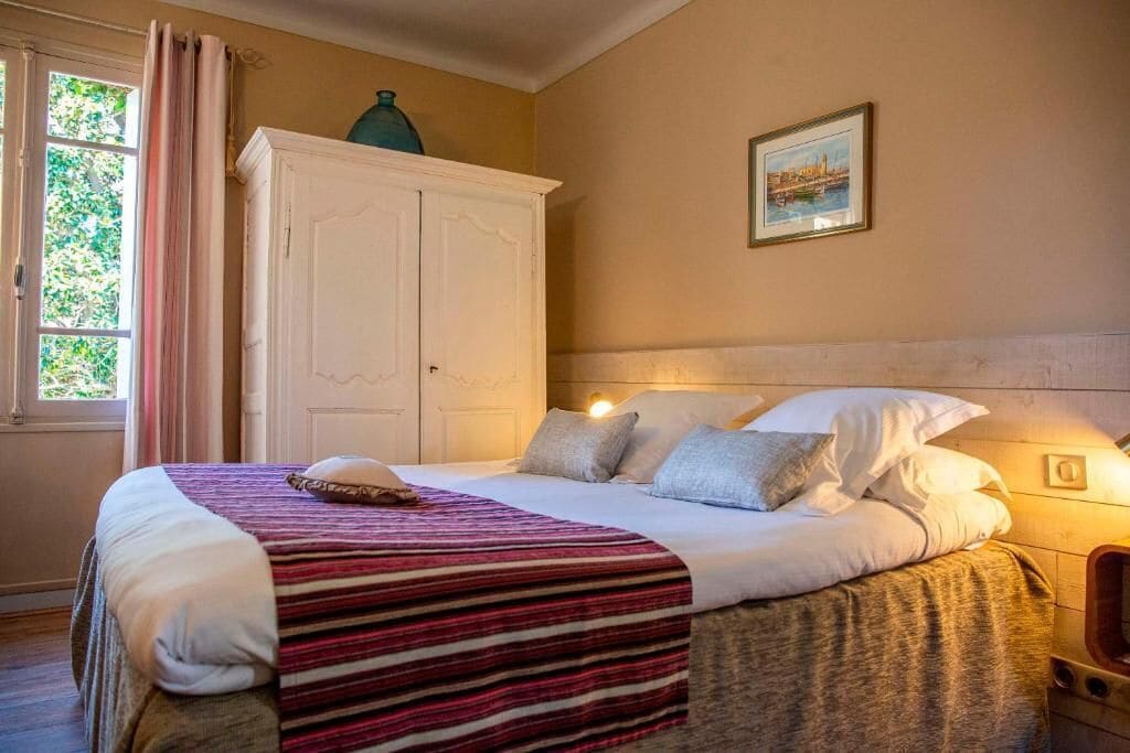 Una cama bien hecha con una colcha a rayas, cabecera blanca y ventana con cortinas.