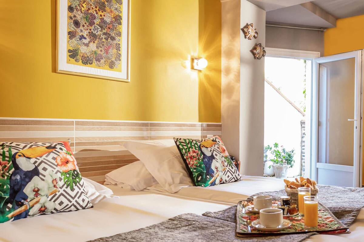 Une chambre d’hôtel avec un lit, des oreillers, un plateau avec des articles pour le petit-déjeuner et une fenêtre avec des rideaux.