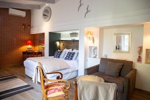 Un dormitorio con cama, una silla de madera, un sofá, una mesita con lámpara y un espejo en la pared.