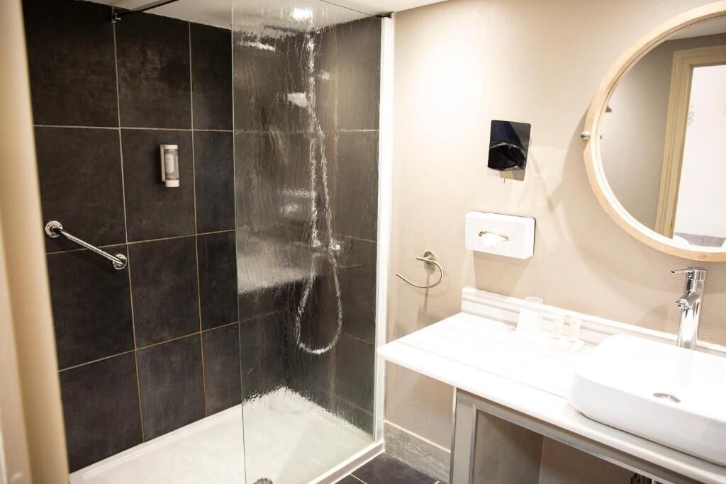 A modern bathroom with a glass-enclosed shower, a white sink, and a round mirror.