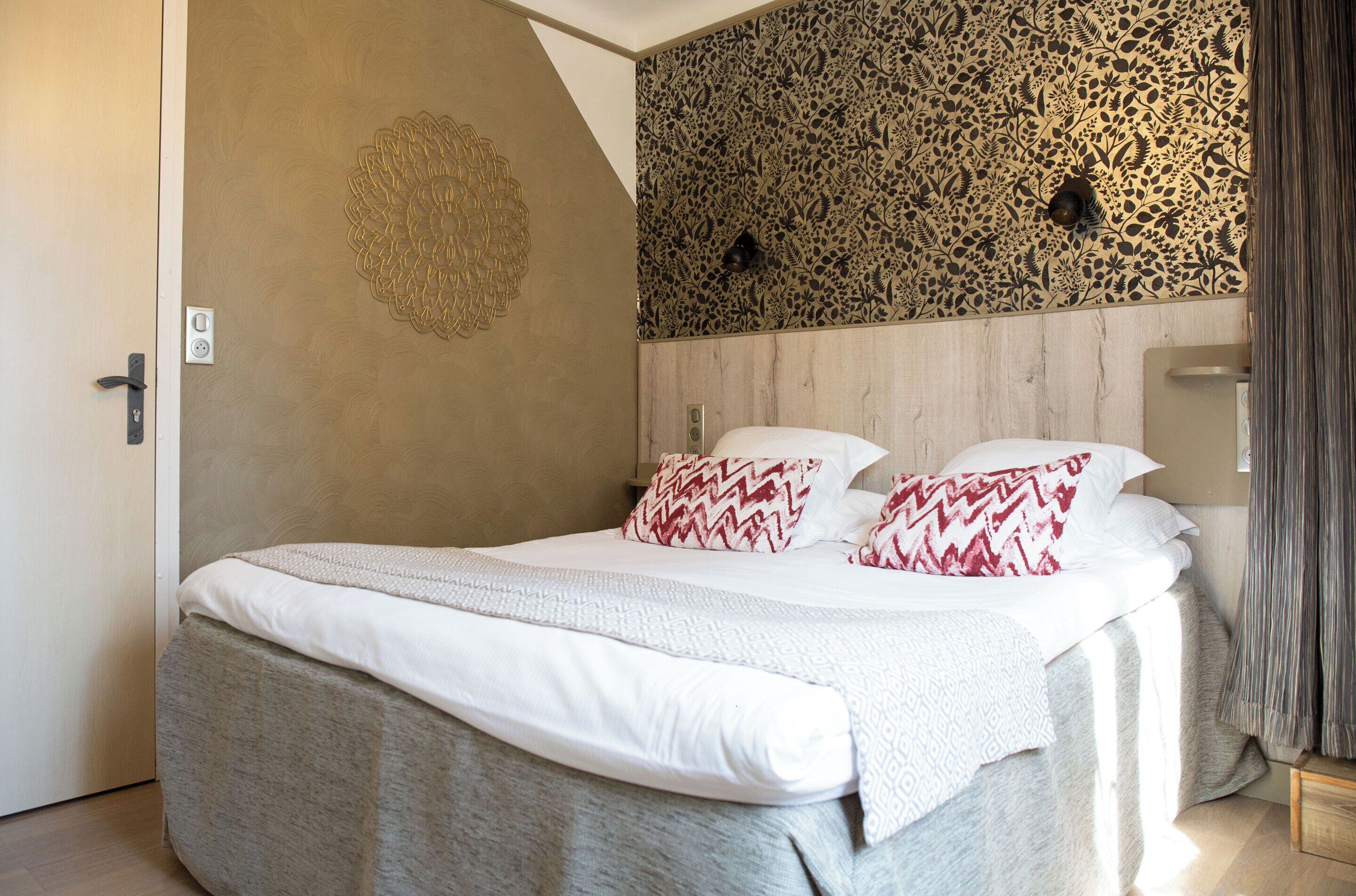 Ein ordentlich bezogenes Bett mit gemusterten Kissen, eine dekorative Wand und ein Lichtschalter.