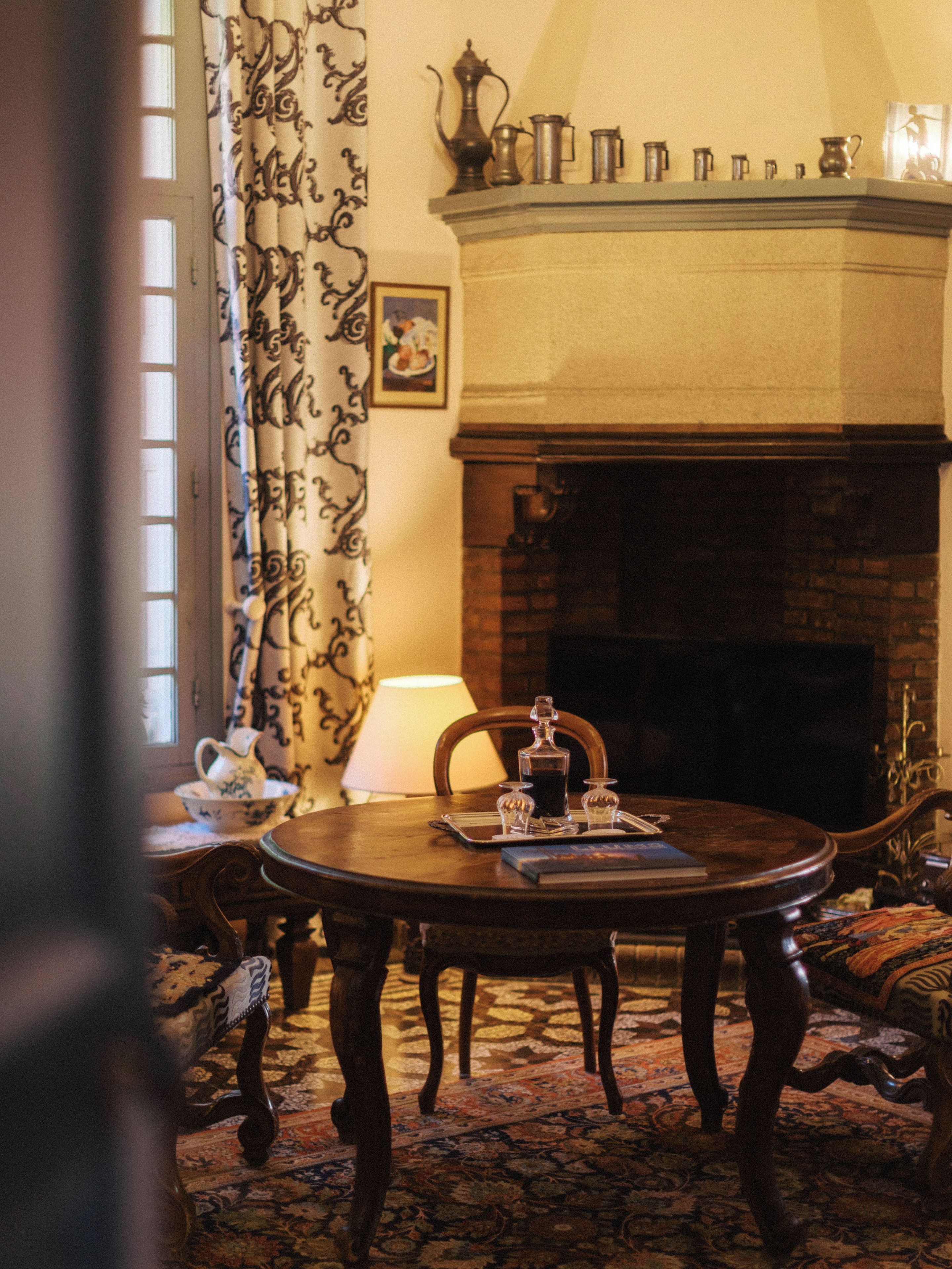 Une pièce au décor traditionnel, avec une cheminée, une table ronde en bois et des rideaux à motifs.