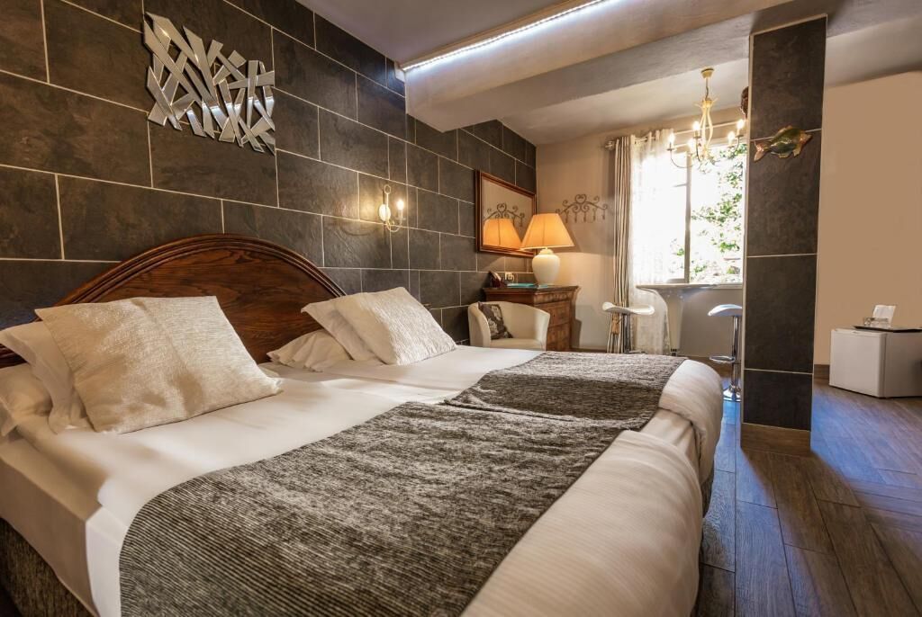 Una habitación de hotel con una cama grande, una mesita de noche, una lámpara y una ventana con cortinas.
