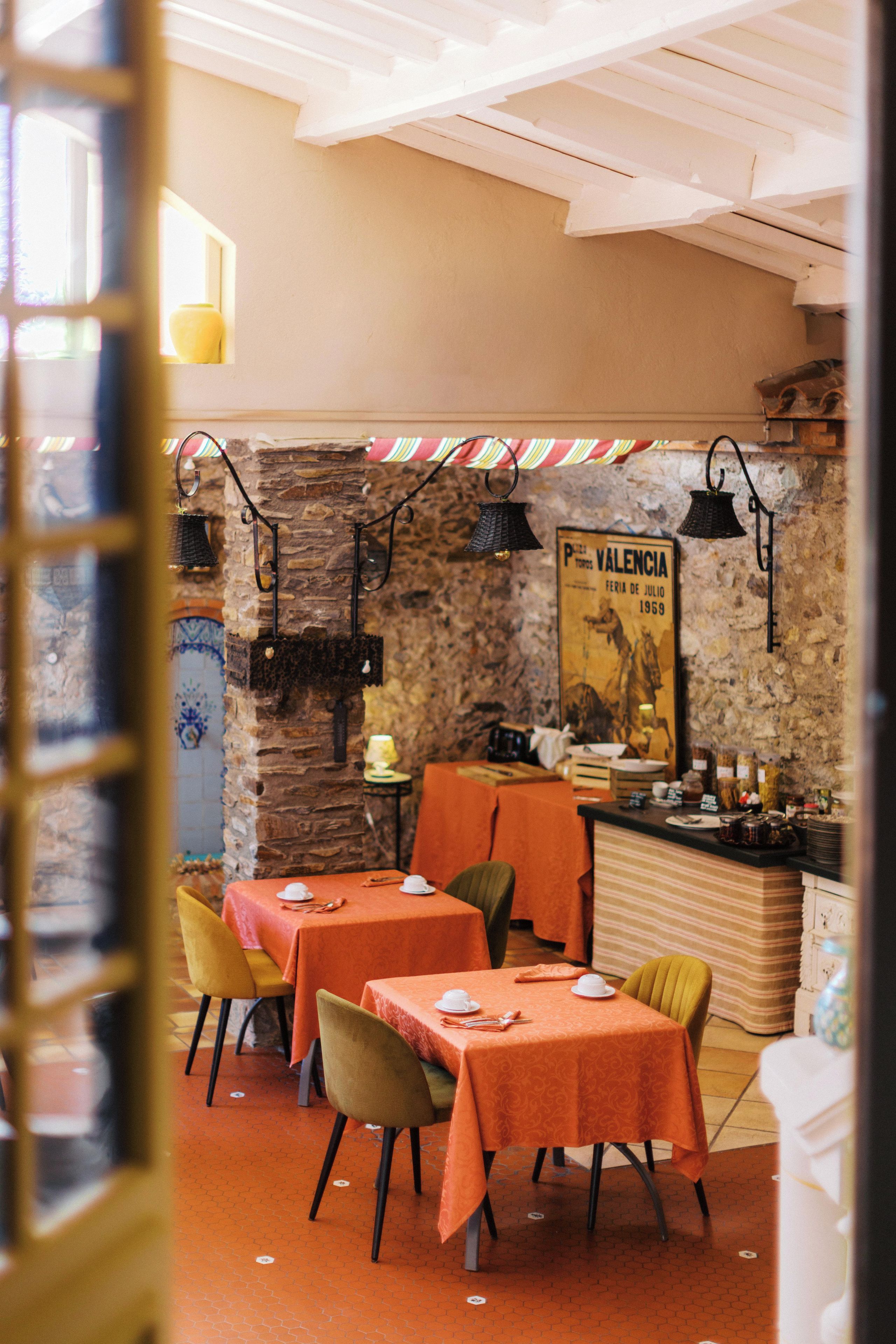 L’intérieur d’un restaurant avec des murs en pierre, des nappes orange et des lampes suspendues noires.