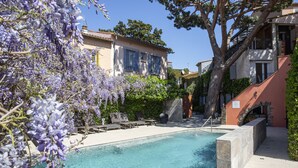 A swimming pool with a clear blue water, surrounded by lounge chairs and purple flowering trees. - Hôtel La Casa Païral (Collioure)