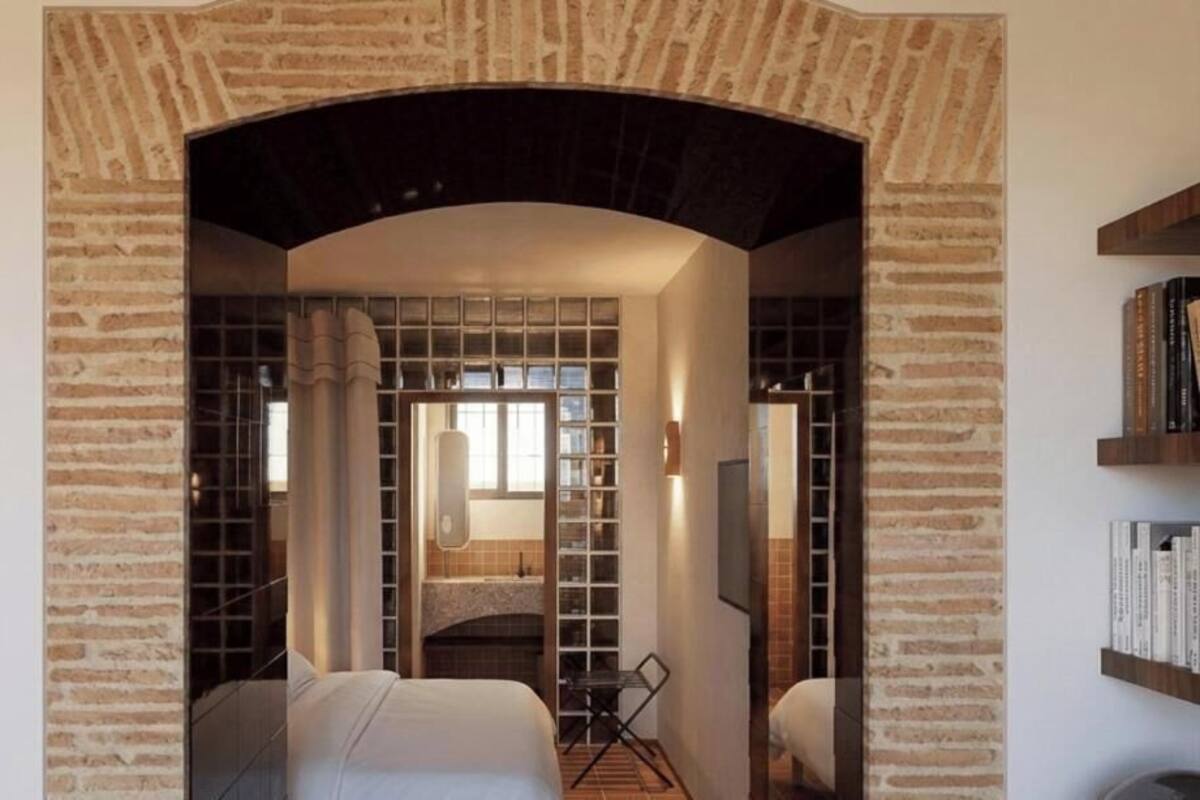 Une chambre d’hôtel avec une arche en briques, un lit, un bureau et une bibliothèque.