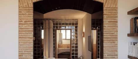 Habitación de hotel con un arco de ladrillo, una cama, un escritorio y una estantería.