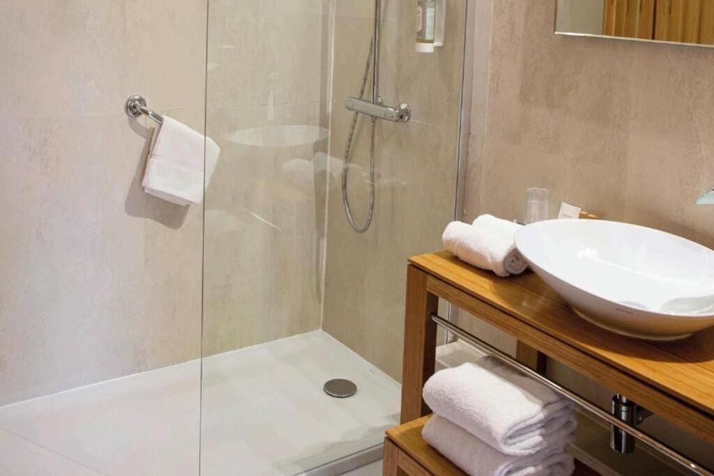 Un baño moderno con cabina de ducha de vidrio, tocador de madera con un lavamanos grande y toallas ordenadas.