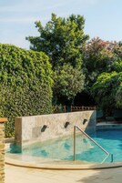 Una piscina con pared de piedra y barandillas metálicas, rodeada de abundante vegetación y árboles.