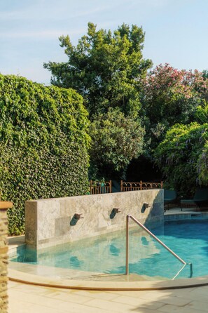 Una piscina con pared de piedra y barandillas metálicas, rodeada de abundante vegetación y árboles.