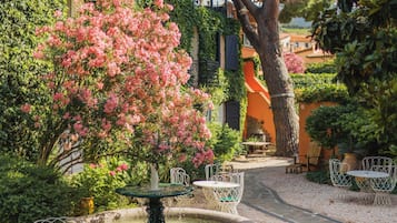 A garden with a fountain, a pathway, and a building with a balcony.