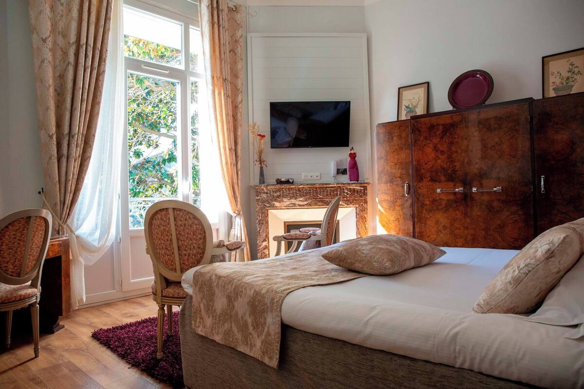 Une chambre à coucher avec un lit, un téléviseur fixé au mur, une armoire et une fenêtre avec des rideaux.